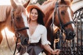 A girl in a white dress and hat walks with horses in nature .A stylish woman stands next to horses near the estate Royalty Free Stock Photo