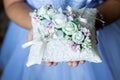 Girl in white dress is holding gold wedding rings on a white pillow with white ribbon and roses.