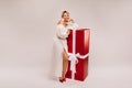 A girl in a white dress with a huge red gift on a white background smiles