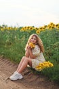 a girl is sitting on the edge of a dirt road with sunflower flowers Royalty Free Stock Photo