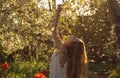 Girl in white dress sitting among flowers and fluff with threw back her head near tulips in sunset, dandelions and cherry flowers