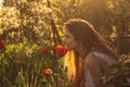 Girl in white dress smelling tulip in sunset among fluff, dandelions and cherry flowers Royalty Free Stock Photo