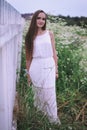 A girl in a white dress is standing in a field by the fence Royalty Free Stock Photo