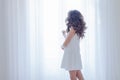 Girl in white dress stands at the window Royalty Free Stock Photo