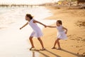 Girl in white dresses playing on beach. older sister pulls younger into water