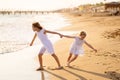 Girl in white dresses playing on beach. older sister pulls younger into water