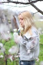 A girl with white hair, in a transparent jacket, stands near a blossoming tree with white tulips. Spring mood