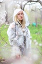 A girl with white hair, in a transparent jacket, stands near a blossoming tree with white tulips. Spring mood