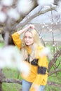 A girl with white hair, in a Yellow sweater, stands near a blossoming tree with daffodil flower. Spring