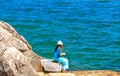 A girl in a white hat is fishing near a cliff near the sea in Kotor Bay.