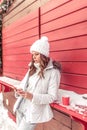 A girl in white jumpsuit and jacket in winter hat. Standing at red wooden counter in his hand holding phone. A woman Royalty Free Stock Photo