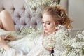 Girl white light dress and curly hair, portrait of woman with flowers at home near the window, purity and innocence. Curly blonde Royalty Free Stock Photo