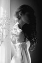 Girl white light dress and curly hair, portrait of woman with flowers at home near window, purity and innocence. Curly blonde Royalty Free Stock Photo