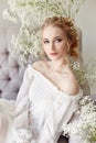 Girl white light dress and curly hair, portrait of woman with flowers at home near the window, purity and innocence. Curly blonde Royalty Free Stock Photo