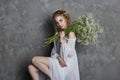 Girl white light dress and curly hair, portrait of woman with flowers at home near the window, purity and innocence. Curly blonde