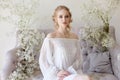 Girl white light dress and curly hair, portrait of woman with flowers at home near the window, purity and innocence. Curly blonde Royalty Free Stock Photo