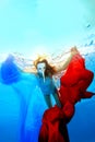 Girl in a white mask with a long nose swims underwater and plays with red and blue fabrics. Royalty Free Stock Photo