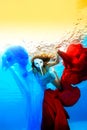 The girl in the white mask swims underwater and plays with red and blue cloth on a background of sunset. Royalty Free Stock Photo