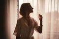 A girl in a white satin dressing gown with a neckline and a manicure french holds a bottle with perfume and splashes on her wrist Royalty Free Stock Photo