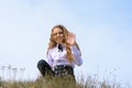 A girl in a white shirt with a bow tie sits on the ground in a field against the background of the sky and waves a pen to the Royalty Free Stock Photo