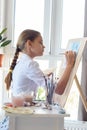 Girl in white shirt draws behind easel with right hand