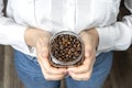 A girl in a white shirt and holds in her hands a glass jar with coffee beans