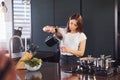 Girl in white shirt standing indoors in kitchen and poring water into glass Royalty Free Stock Photo