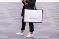 Girl with white sneakers standing holding a Gucci shopping bag on a street.