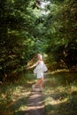 A girl in a white suit and a funny children`s hairstyle walks in the park, runs along the path and screams Royalty Free Stock Photo