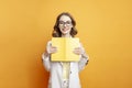 girl in white suit holds book on colored background, female student in blazer teaches lessons, teacher with yellow book