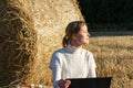 Girl in a white sweater against the background of a haystack with a laptop in her hands sits on the ground Royalty Free Stock Photo