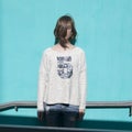 Girl in a white sweater dreamily closes her eyes from the bright sun opposite the blue wall in the underpass Royalty Free Stock Photo