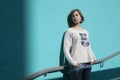 Girl in a white sweater dreamily closes her eyes from the bright sun opposite the blue wall in the underpass Royalty Free Stock Photo