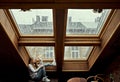 A girl in a white sweater looks up, touching the window in the ceiling of the house with one hand