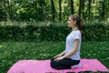 A girl in a white T-shirt and black leggings sits on a pink mat on a summer green lawn