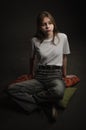 Girl in white t-shirt on dark background sitting on the floor on pillows Royalty Free Stock Photo