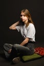 Girl in white t-shirt on dark background sitting on the floor on pillows Royalty Free Stock Photo