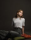 Girl in white t-shirt on dark background sitting on the floor on pillows Royalty Free Stock Photo