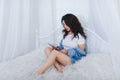 Girl in a white t-shirt and denim shirt, sits on the bed and uses a laptop. Royalty Free Stock Photo