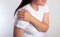 A girl in a white T-shirt is holding her shoulder joint and is in severe pain. Concept of habitual shoulder dislocation