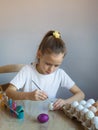 A girl in a white T-shirt paints Easter colored eggs with paints and a brush close-up. Spring.The child holds the painted eggs. Royalty Free Stock Photo