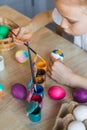 A girl in a white T-shirt paints Easter colored eggs with paints and a brush close-up. Spring. The child holds the painted eggs. Royalty Free Stock Photo