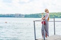 Girl in white T-shirt and skirt in sunglasses on small wooden pier on shore of lake