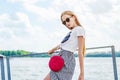 Girl in white T-shirt and skirt in sunglasses on small wooden pier on shore of lake