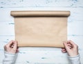 Girl in a white warm sweater unwinds a roll of wrapping paper to wrap a padarok for a new year Christmas, on a wooden rustic ba Royalty Free Stock Photo
