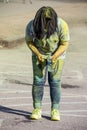 Girl who has been working squirting powder on runners in holi color run and is covered with colored powder bends over washing her Royalty Free Stock Photo