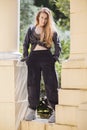 A girl in wide pants and a shirt tied with a knot stands between the columns in the park Royalty Free Stock Photo