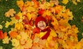 A girl with a wide smile lies on a carpet of red and yellow leaves in an autumn park. Royalty Free Stock Photo