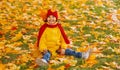 A girl with a wide smile is sitting on a carpet of red and yellow leaves in an autumn park. Royalty Free Stock Photo