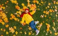 A girl with a wide smile is sitting on a carpet of red and yellow leaves in an autumn park. Royalty Free Stock Photo